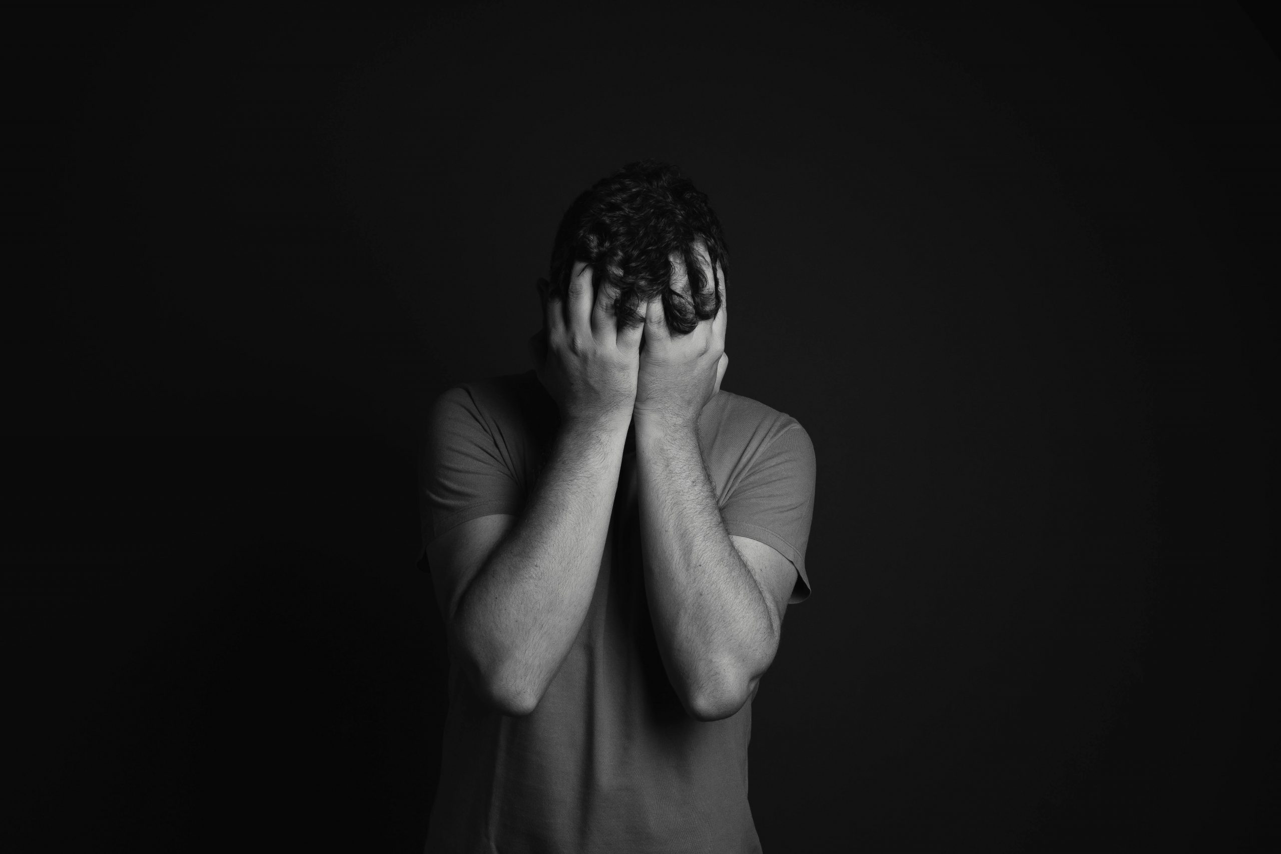 A grayscale portrait of a man covering his face, depicting emotion and mental health themes.